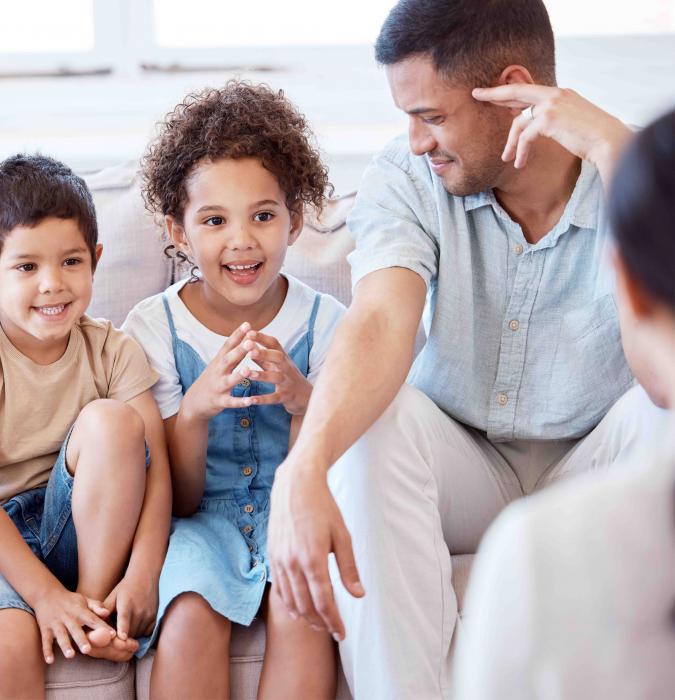 A family sits on a couch in a sunny room while speaking to a therapist. 